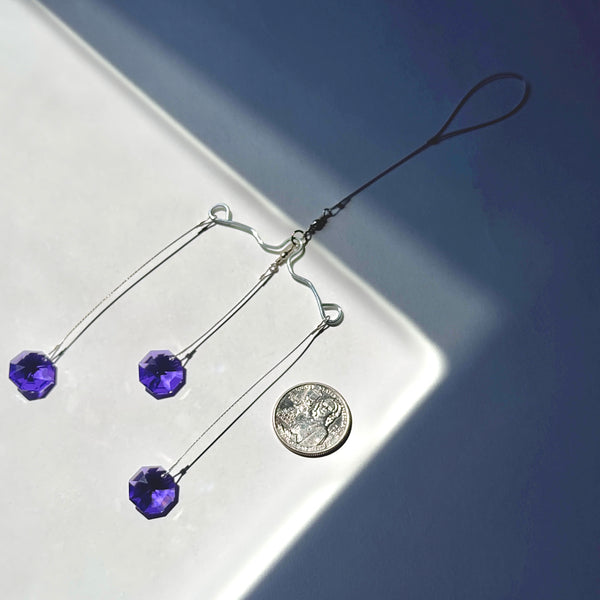 Silver earring with purple gemstones and a coin charm on a reflective surface.